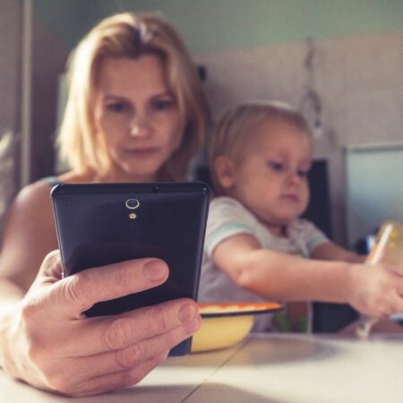 Woman with young children either side, looking at her mobile and seeming stressed.
