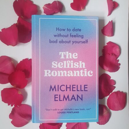Picture of the book The Selfish Romantic, with its pastel pink and blue front cover, surrounded by red rose petals.