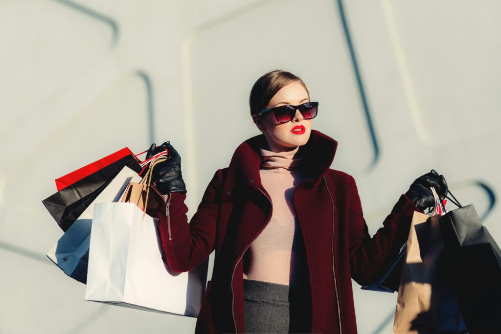 Woman with brown hair tied back and sunglasses holding an array of shopping bags.