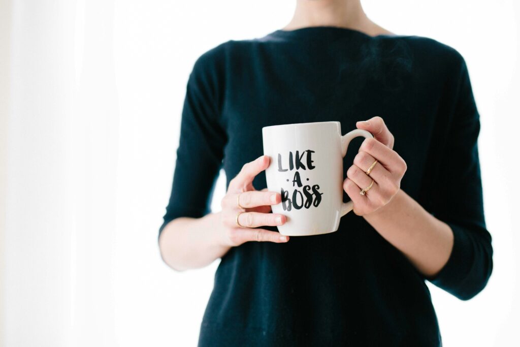Woman in black jumper, with red nails, holding a cup that says like a boss on it.