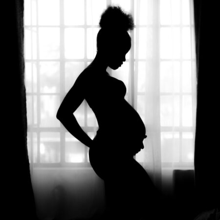 Pregnant woman posing in silhouette by a window.