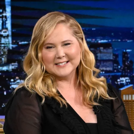 Amy Schumer in a black dress with blonde hair on the Jimmy Fallon Show.
