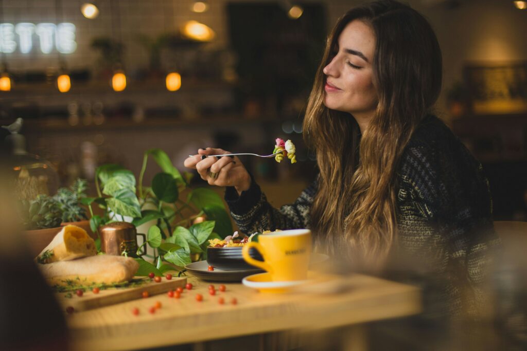 Woman with long brown hair and eyes closed, enjoying her pasta salad.