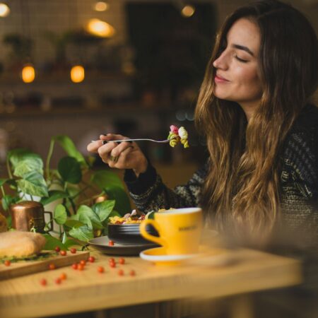 Woman with long brown hair and eyes closed, enjoying her pasta salad.